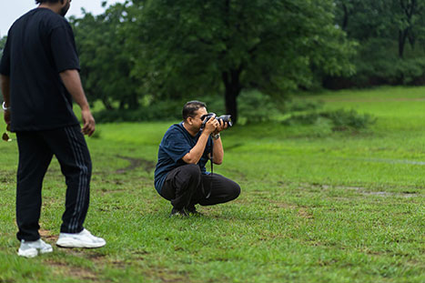 Ankit Tiwari, a photographer, crouches in green grass with a camera, focusing on the Pachmarhi Monsoon Marathon amidst misty weather in Satpura Hills, highlighting documentary sports photography challenges.