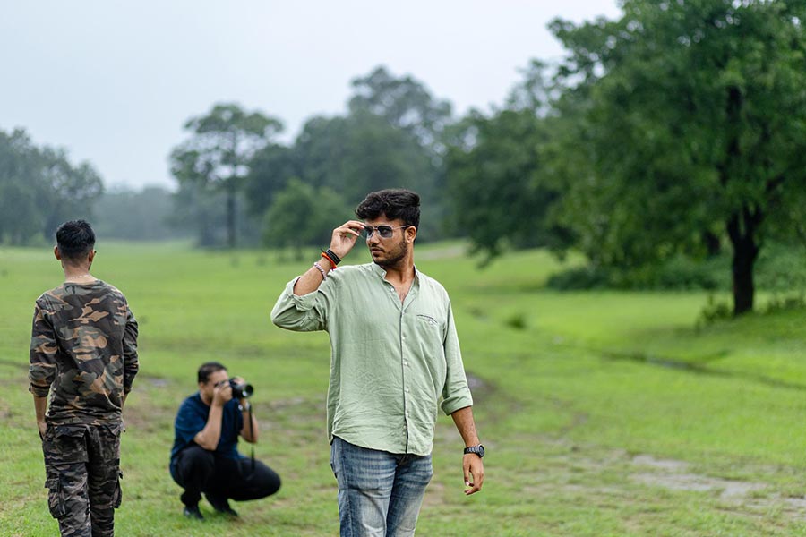 Jai Tripathi, a drone photography professional, adjusts his sunglasses while standing in a wide green field during the Pachmarhi Monsoon Marathon shoot, with other team members in the background.