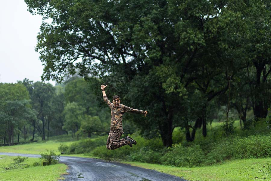 Kuldeep Lodhi, a drone photography professional, jumps joyfully in the air on a wet road surrounded by green trees during the Pachmarhi Monsoon Marathon in Madhya Pradesh.
