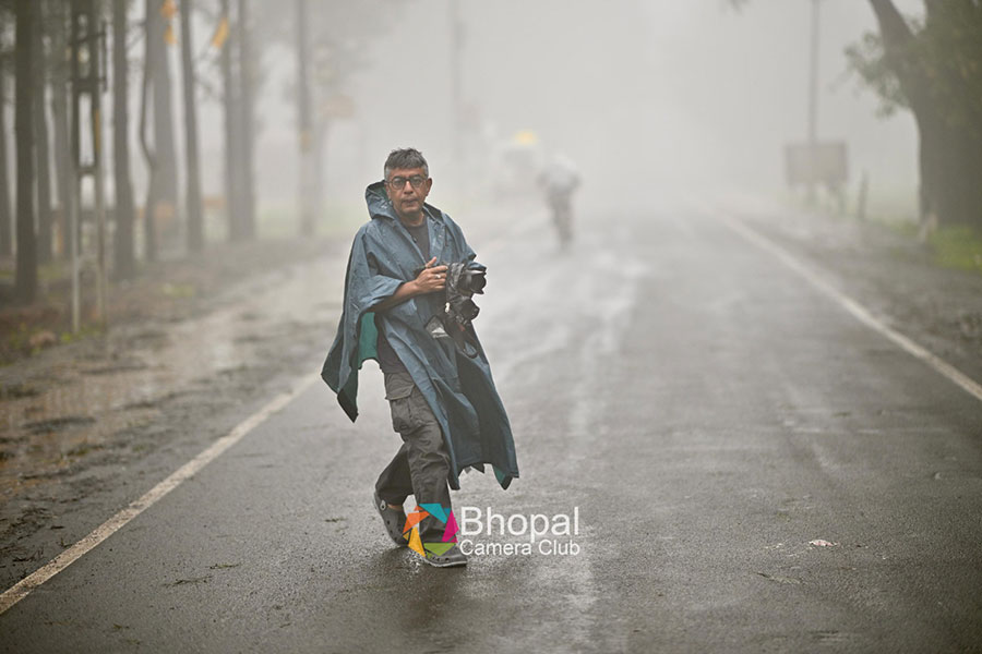 Sauvik Acharyya, a commercial and documentary photographer from Bhopal, Madhya Pradesh, walks on a misty, wet road in a rain poncho, holding a camera, during the Pachmarhi Monsoon Marathon in the Satpura Hills.
